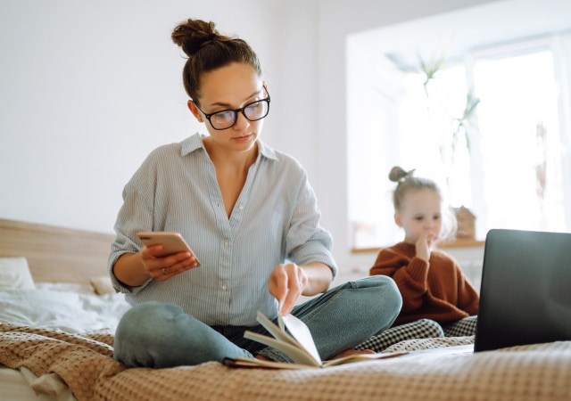 Parent sitting with child on bed while trying to get work done