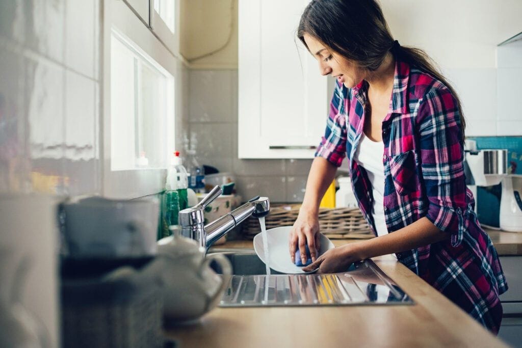 Young woman washing dishes and doing a list of household chores