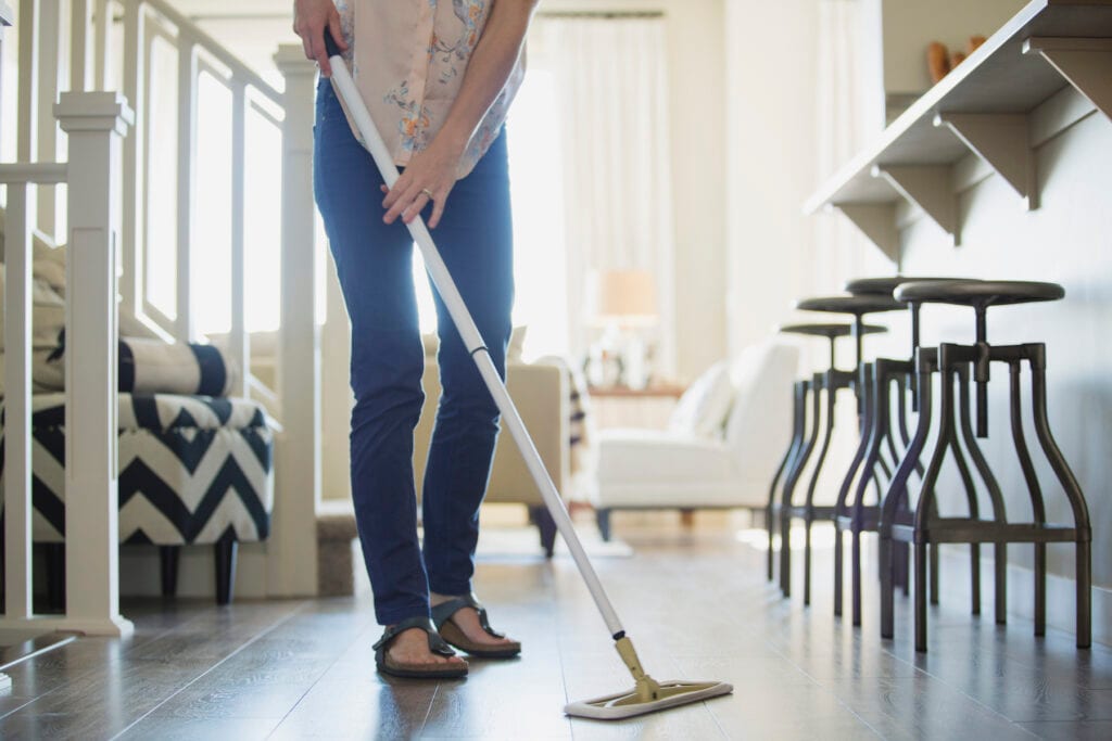 Young woman dusting floor and doing a list of household chores