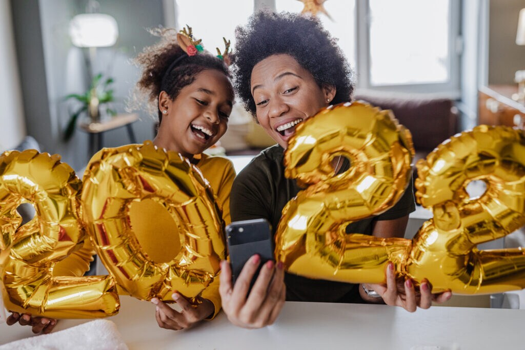 Mother and daughter are at home, they are holding 2022 new years eve balloon numbers and taking a selfie