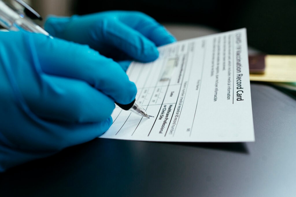 Hand of Doctor wearing surgical glove to certify Vaccination card and passport for Covid-19 (coronavirus) vaccine