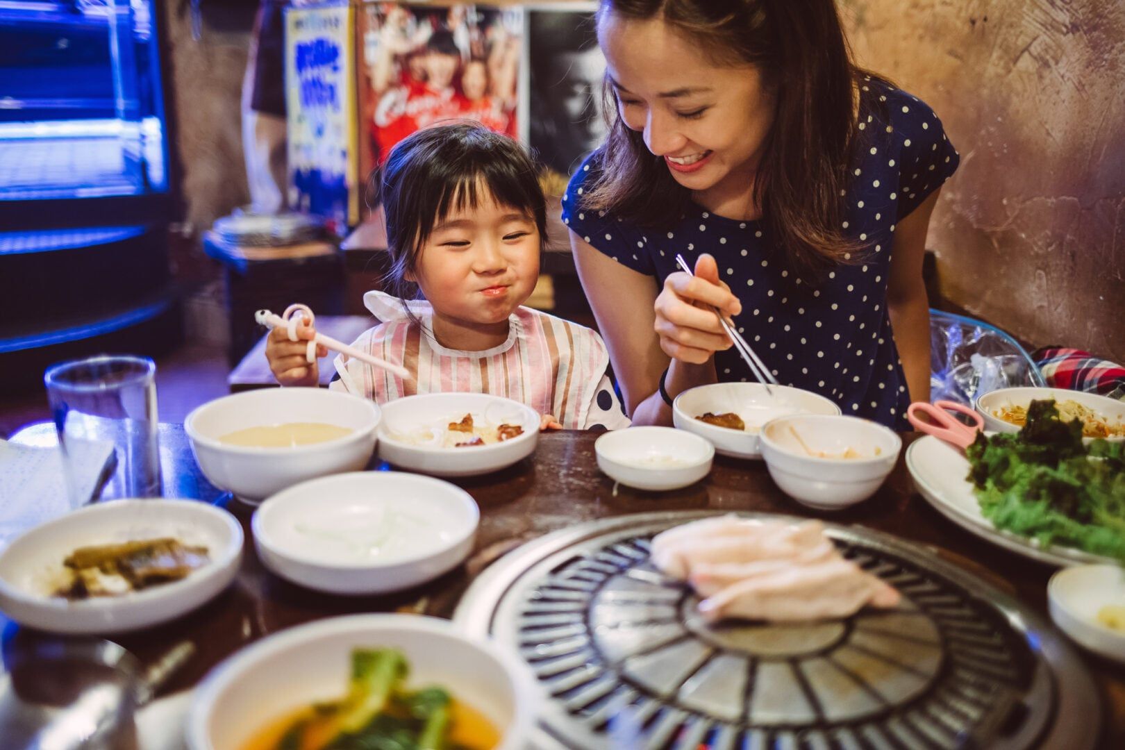 Nanny talking joyfully with lovely little girl while having Korean BBQ dinner in a restaurant